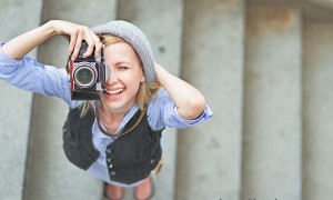 Happy hipster girl making photo with retro camera on city street
